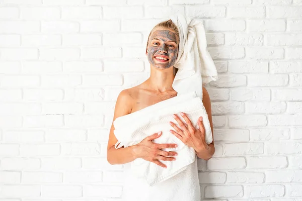 Spa Facial Mask. Spa and beauty. Young smiling woman holding white bath towels with a clay facial mask on her face