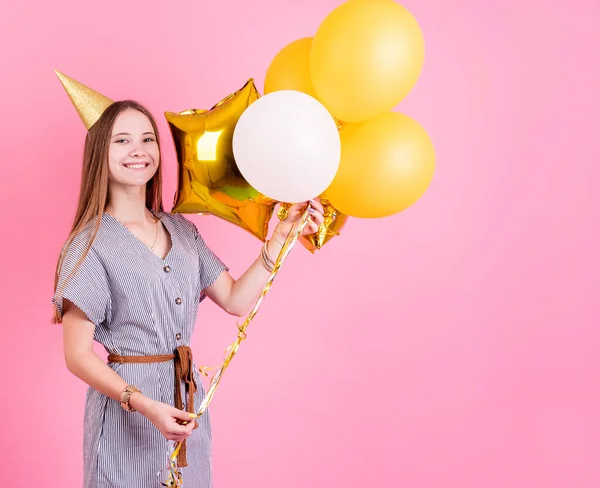 Mujer joven en un sombrero de cumpleaños sosteniendo globos y caja de regalo grande celebrando fiesta de cumpleaños — Foto de Stock