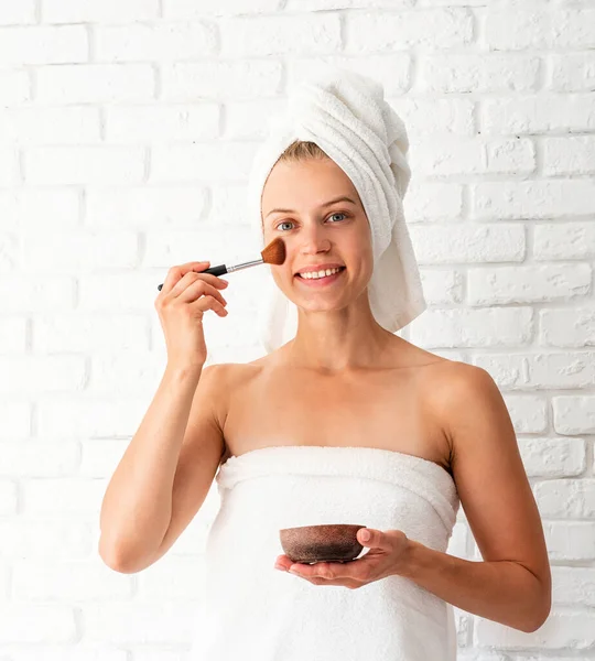 Wanita cantik muda mengenakan handuk putih mengoleskan scrub di wajahnya — Stok Foto