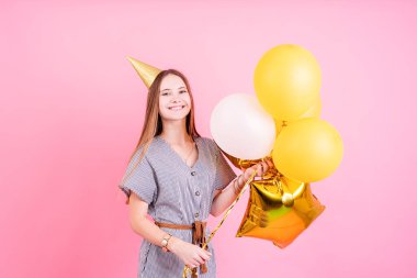 Doğum günü partisi. Doğum günü şapkalı genç bir kadın elinde balonlar ve büyük bir hediye kutusu var. Doğum günü partisini pembe arka planda fotokopi çekerek kutluyorlar.