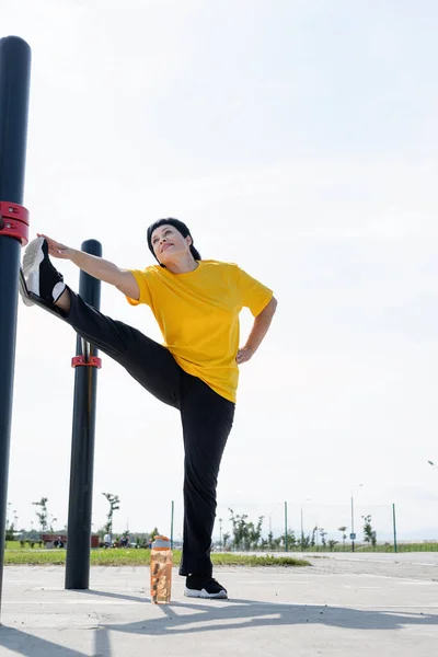 Mujer mayor estirando sus piernas al aire libre en el campo de deportes — Foto de Stock