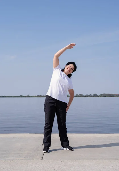 Mujer mayor activa y feliz haciendo ejercicio cerca de la orilla del río — Foto de Stock