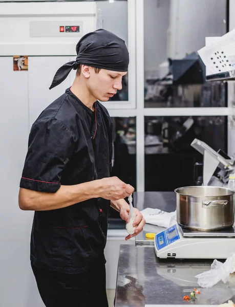 Young cook in black uniform working at the kitchen of the restaurant
