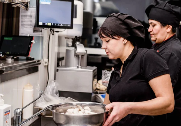 women bakers in black uniform at the pizzeria kitchen working on order