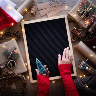 Zero waste and eco friendly christmas concept. Female hands holding blank letter board with christmas gifts and eco friendly decorations top view flat lay clipart
