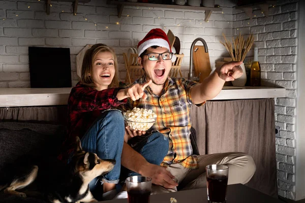 Jeune couple regardant des films à la maison à Noël pointant vers l'écran — Photo