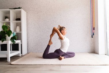 Sağlıklı bir yaşam tarzı. Yoga yapan, spor giyimli, beyaz gömlekli, mor pantolonlu, uzun boylu, gri arka planlı genç, çekici bir kadın.