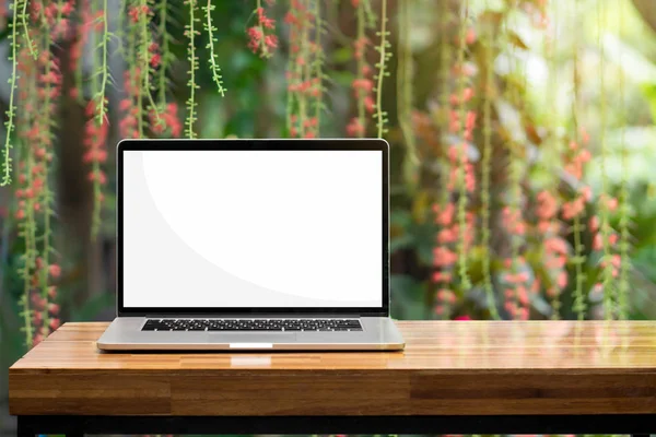 Laptop leeg scherm op houten tafel rode bloemen groene tuin Stockfoto