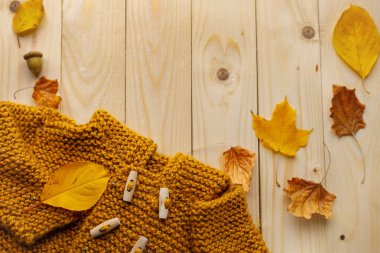 Sonbahar yaprakları ve meşe palamudu ile çevrili, ahşap düğmeli, rahat örülmüş sarı bir süveterin düz kompozisyonu. Sıcak sonbahar atmosferi, mevsimsel moda ve kırsal tarz.