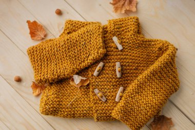 Doğal ahşap arka planda sonbahar akçaağaç yapraklarıyla süslenmiş hardal sarısı renkte el yapımı, düz bir süveter. Mevsimsel kırsal yaşam sonbahar modası ve yaşam tarzı içindir..
