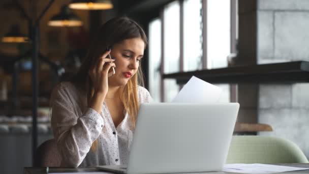 Boldog üzletasszony, beszél a telefonon, egy kávézóban, és gépelés-ra egy laptop — Stock videók