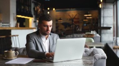 Gri takım elbise giymiş, kafede masada oturan ve dizüstü bilgisayar kullanarak işadamı Genç sakallı
