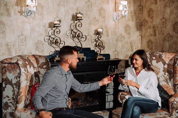 Молодая пара в ресторане сидит в креслах у камина и пьет вино — стоковое фото