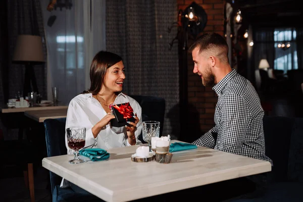 Sorprendido mujer feliz sentado junto a la mesa en la fecha en la cafetería y recibe el regalo . — Foto de Stock