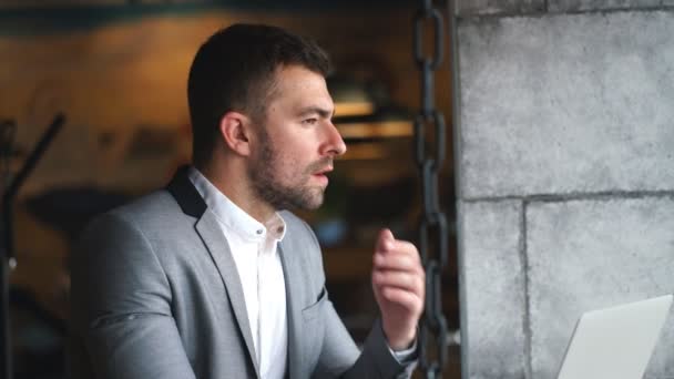 Un jeune homme d'affaires en costume gris et une chemise blanche travaille dans un ordinateur portable dans un café — Video