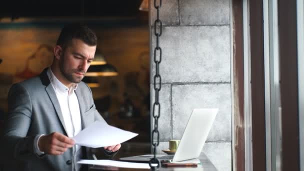 Joven hombre de negocios guapo relajarse en la cafetería durante el desayuno, escribiendo en el ordenador portátil genérico mientras revisa el correo electrónico o mensajería en línea — Vídeos de Stock