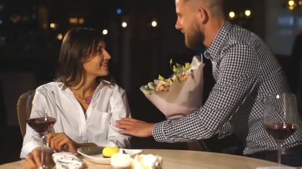 Feliz pareja romántica en el café. Joven hombre está presentando flores a su amada . — Vídeos de Stock
