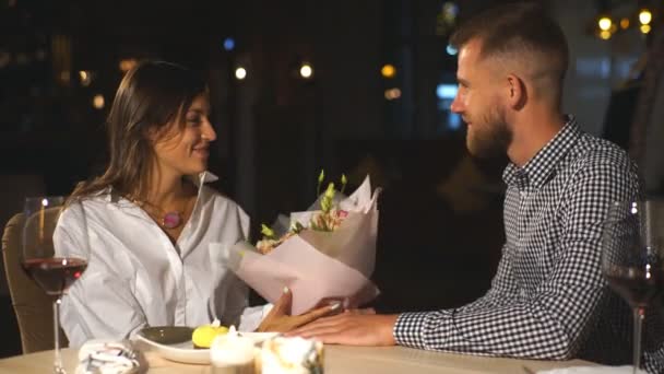 Красивий молодий чоловік дарує подарунок і квіти красивій жінці в кафе — стокове відео