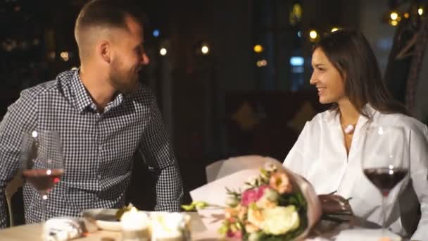 Красивая брюнетка делает подарок своему парню в ресторане на свидании — стоковое видео