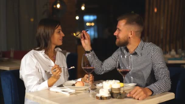 Pareja joven en una cita. Un hombre alimenta a su mujer con un delicioso postre. Pareja riendo en el restaurante — Vídeos de Stock