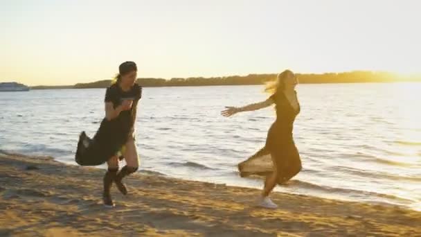 Zwei Mädchen in einem schwarzen Kleid spazieren am Strand entlang und tanzen — Stockvideo