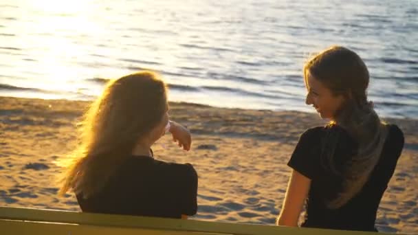 Duas jovens mulheres no banco admirando o pôr do sol — Vídeo de Stock