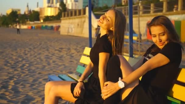 Két fiatal nő a padon, hogy megcsodálja a naplementét, és pózol — Stock videók