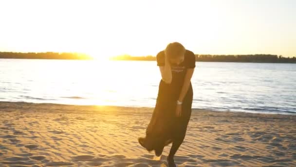 Mooie jonge vrouw dansen op het strand en poseren op camera in zwarte jurk — Stockvideo