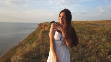 beyaz bir sundress güzel bir esmer bir uçurum kameraya poz onun elinde şapka ile