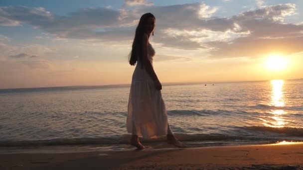 Mujer joven en vestido de sol caminando en la playa al atardecer — Vídeo de stock