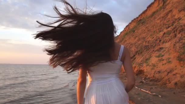 Mooie brunette met lange haren die op het strand bij zonsondergang achtergrond worden uitgevoerd — Stockvideo