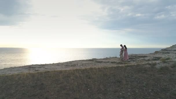 Vista aérea de los recién casados ir de la mano y riendo, sobre el fondo de las rocas y el claro verde . — Vídeos de Stock