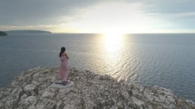 Uzun pembe havadan görünümü kadın elbise sallayarak Denizi yukarıdan manzaralı uçurumun kenarında duruyor