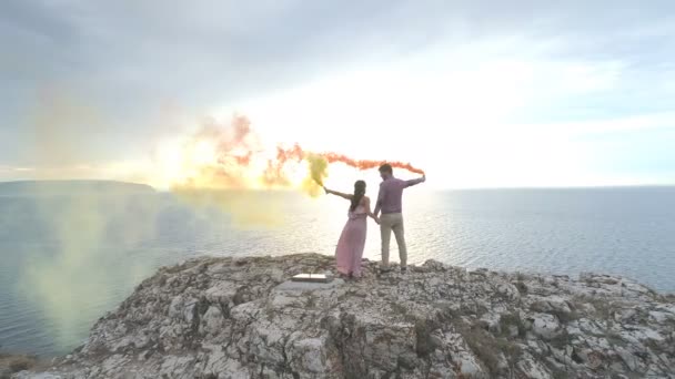 Letecký pohled na milující pár stojí na strmé skále a multi-barevné dýmovnice hoří — Stock video