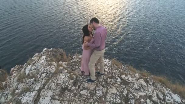 Vista aérea em casal posando e apreciando a bela paisagem na borda das falésias de pedra sobre o grande rio ao pôr do sol em um vento forte — Vídeo de Stock