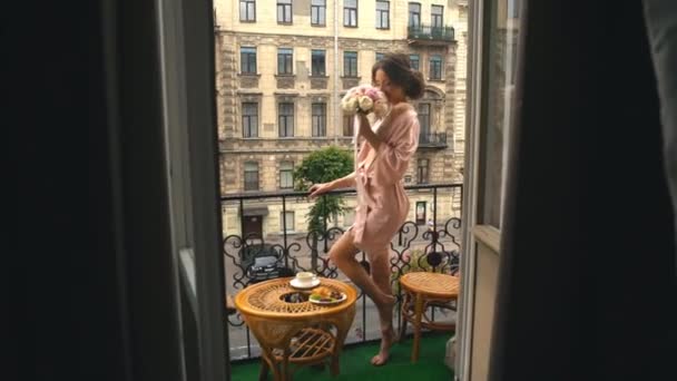 Schöne Braut in einem Seidengewand, die mit einem Strauß auf dem Balkon steht und herumalbert — Stockvideo