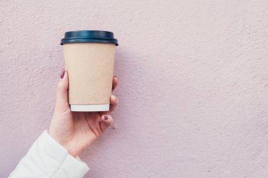 pembe duvar arka plan üzerinde siyah kapaklı kahverengi karton bardak kahve el tutar