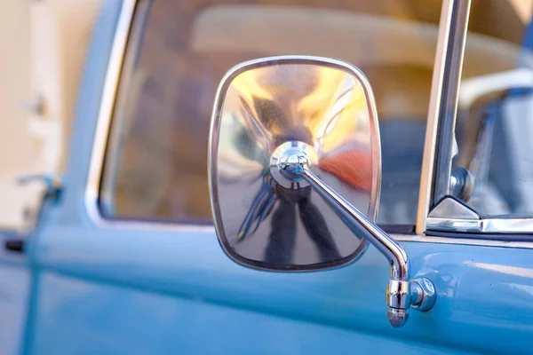 Close up the side mirror of a blue old car. Rear view mirror