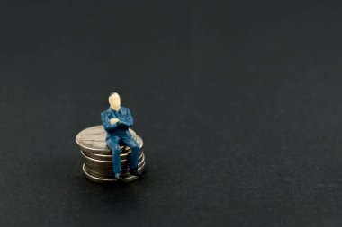 Bir kişi para birikimi dahil kavramı. Oyuncak adam bir yığın sikke siyah bir arka plan üzerinde oturuyor.