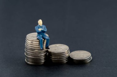 Kişisel sermaye kavramı. Bir yığın sikke siyah bir arka plan üzerinde oturan oyuncak adam.