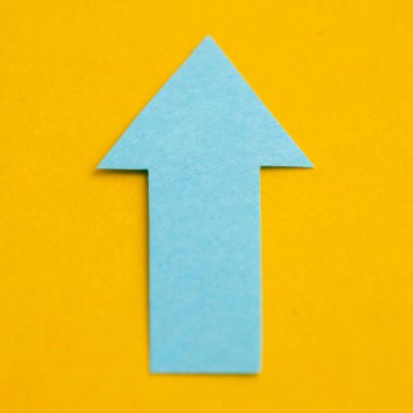 Blue arrow made of paper on a yellow background.