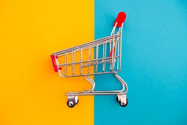 Alışveriş kavramı. Mavi ve sarı zemin üzerine metal arabası. Yakın çekim.