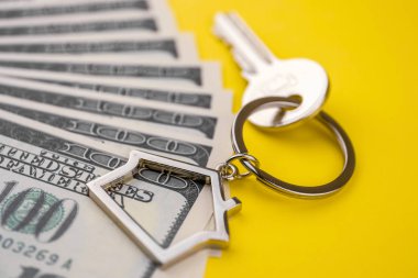 Bir özel ev ya da daire satın kavramı. İpotek kaydı. Para için emlak birikimi. Metal Anahtarlık yüz ABD paketi üzerinde sarı bir arka plan üzerinde dolar yalan bir metal anahtar ile bir ev şeklinde. Yakın çekim.