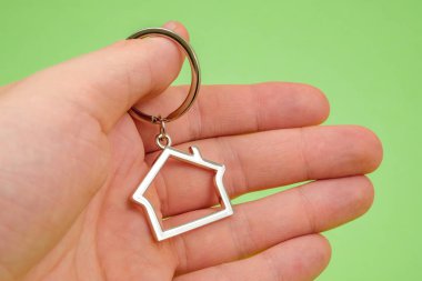 Gayrimenkul veya özel bir ev satın alma kavramı. Bir avuç erkek elinde yeşil bir arka plan üzerinde bir ev şeklinde metal Anahtarlık tutar. Yakın çekim.