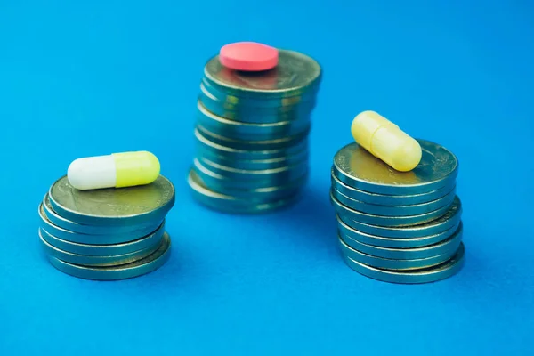 Concept comparison and high cost of drugs. Pink pill and capsule on the stacks of coins on a blue background.