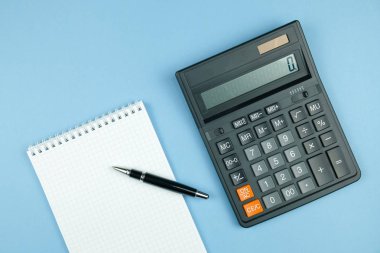 Defter beyaz kağıt ve kalem, mavi arka plan üzerinde siyah büyük hesap makinesi ile kontrol.