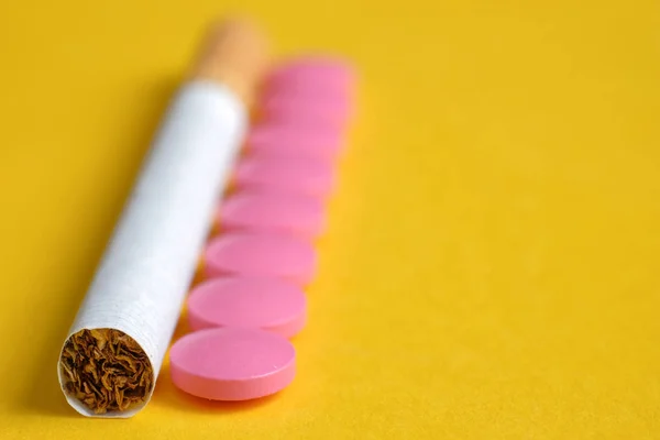 Pink pills for nicotine addiction lies next to a cigarette on a yellow background.