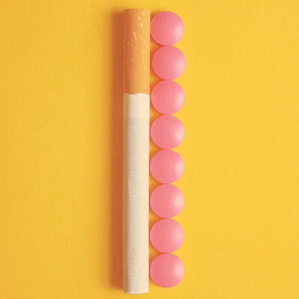 Pink pills for nicotine addiction lies next to a cigarette on a yellow background. Toned. Top view.
