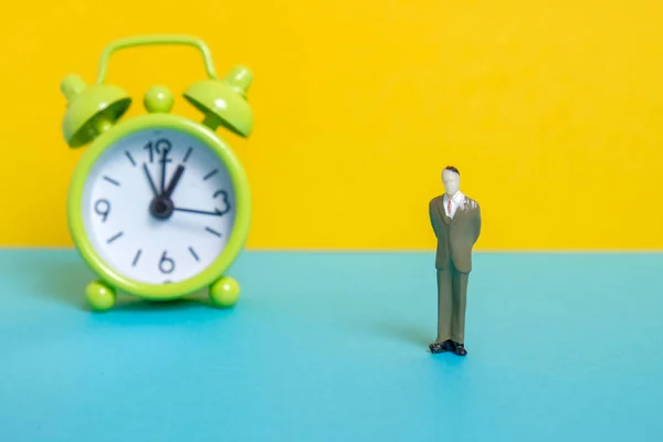 Man dummy next to a green vintage clock on a yellow background.