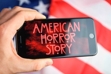Rusya, St.Petersburg - 11 Nisan 2019: Amerikan bayrağının arka planında Screensaver serisi Amerikan korku hikayesi ile bir akıllı telefon tutun.